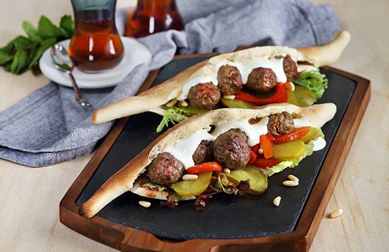 Samoon bread with cream cheese, kofta meatballs, fresh salad leaves, pickled cucumbers and pine nuts