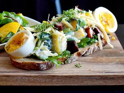 En rustik Grand Sandwich med mer pålägg än bröd. I botten en tunn skiva tyskt surdegsbröd. Bygg på med härliga kontraster av krämigt ägg och salt knaprigt fläsk
blandat med söt beta och syrlig gräddfil. Toppa med smakrik ost och kryddig krasse.
