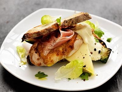 Härlig kycklingburgare med långlagrad Falbygdens Präst®, lufttorkad skinka och stekt zucchini. Att servera allt mellan rostade skivor levain ger en mer rustik karaktär som tilltalar stamgästerna.
