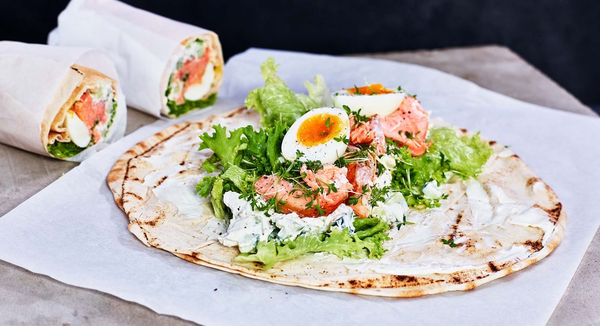 Wrap med varmrökt lax är ett snabbt lunchalternativ för de som är på språng. Det är en mättande och god tunnbrödsrulle med svenska smaker i ett libabröd. Den är fylld med pepparrotskräm med kapris och gurka, kokt ägg, varmrökt lax och krasse. Det blir en uppskattad lunch och är perfekt i caféets eller restaurangens lunchutbud.